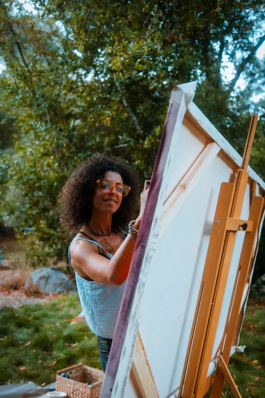 Galeet painting at an easel outdoors, among trees