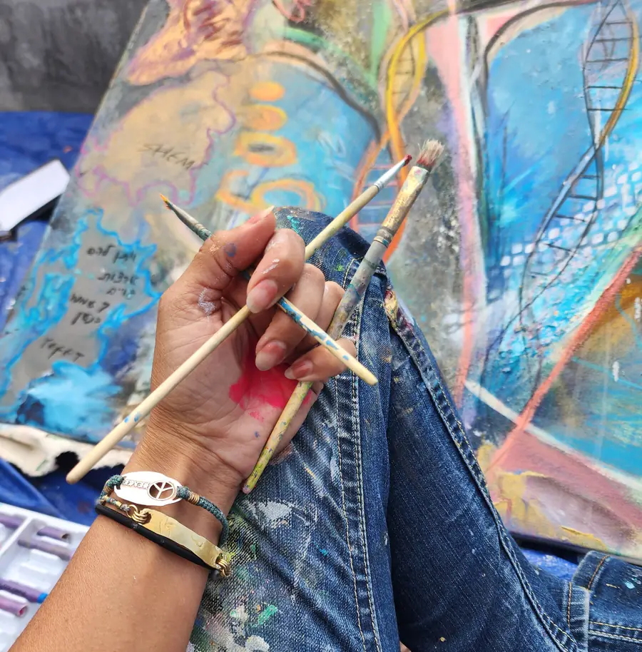 A hand holding paintbrushes over a colorful painting in progress